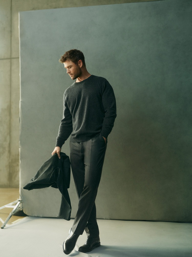Chris Hemsworth wearing dark sweater and trousers holding a jacket in a studio portrait for El Corte Ingles