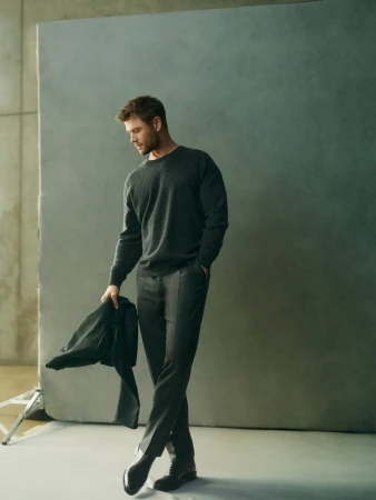Chris Hemsworth wearing dark sweater and trousers holding a jacket in a studio portrait for El Corte Ingles
