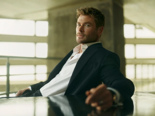 Chris Hemsworth in a dark suit jacket and white shirt seated at a table for El Corte Ingles