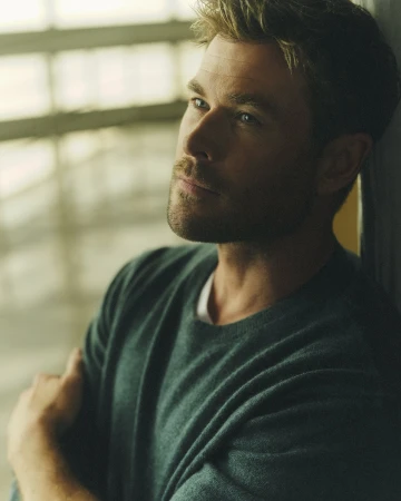 Portrait of a handsome adult man with fair skin and stubble. He has dark blond hair and is wearing a green sweater indoors.