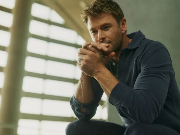 Chris Hemsworth wearing a navy polo shirt with clasped hands against an architectural background for El Corte Ingles