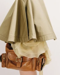 Tan pleated skirt paired with a brown leather shoulder bag against a plain background