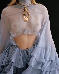 Model wearing a sheer light blue ruffled top with a gold pendant necklace for Chloé Winter 2024 campaign