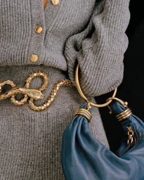 Close-up of grey ribbed knit cardigan and matching skirt worn with a gold snake belt and blue leather handbag