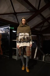 Model wearing a hooded sweater and plaid waist wrap standing backstage during Antonio Marras fall winter collection