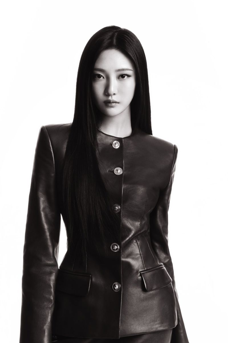 Striking portrait of an adult female with long, straight dark hair in a fitted black leather jacket against a bright white backdrop.