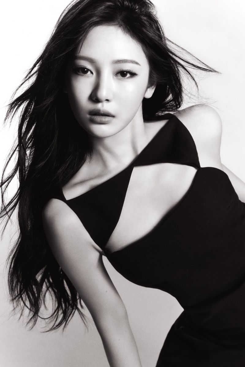 Elegant woman in a black cut-out dress gazes intensely at the camera, with long dark hair cascading against a light backdrop.