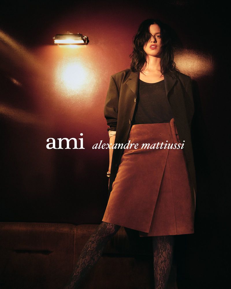 Fashionable woman posing indoors with skirt, jacket, and patterned tights, lit by a spotlight for a high-fashion magazine spread.