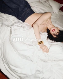 Model lying on white bedsheets wearing denim trousers and a gold cuff bracelet