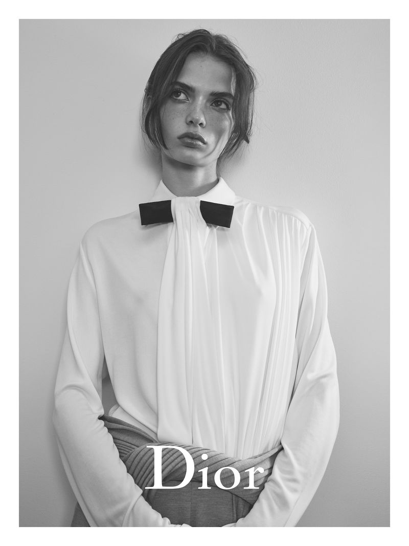 Black and white fashion shot of a female model in a white top and bow tie, posing in front of a neutral background, minimalist aesthetic.