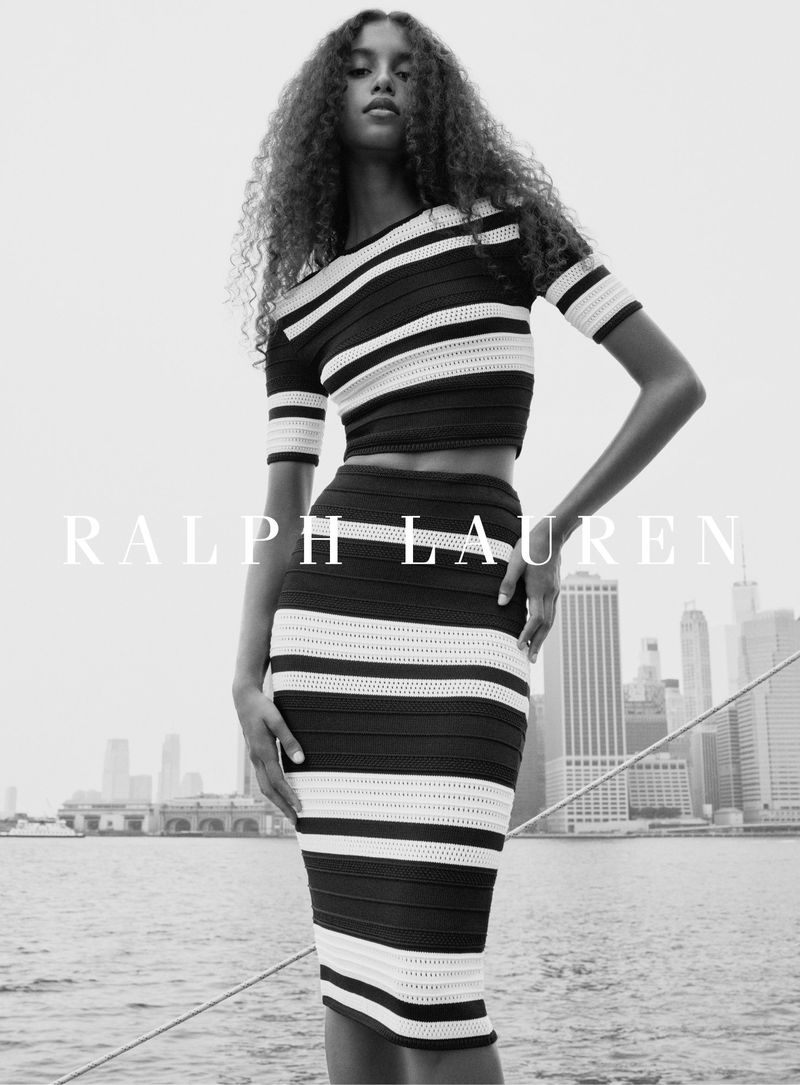 Model in a black and white striped two-piece knit outfit posing against a city skyline and water background