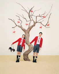 Xiao Wen Ju and Jin Dachuan posing in red Thom Browne cardigans beside a bare tree decorated with hanging red horse ornaments.