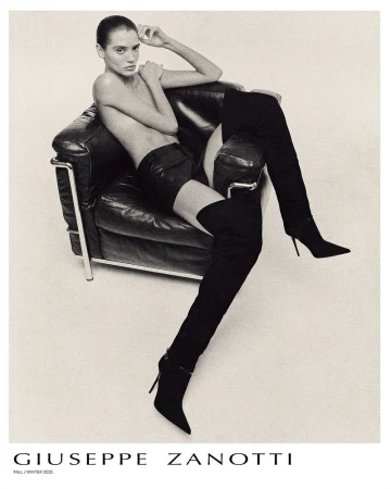 Model Valentina Ferrari reclining in a black leather armchair wearing black thigh-high stiletto boots for Giuseppe Zanotti.