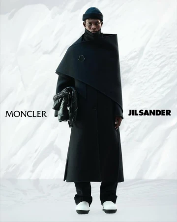 Fashion model in a black coat and beanie, holding a soft black bag against a snowy backdrop, promoting Moncler and Jil Sander.