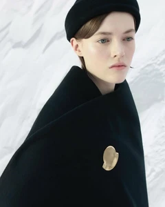 Model wearing a black coat and beret with a gold pin against a snowy backdrop for Moncler x Jil Sander