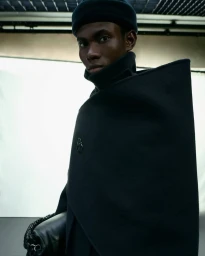 Model Prince Diamond wearing a structured black high-collar cape coat and beanie for Moncler x Jil Sander.