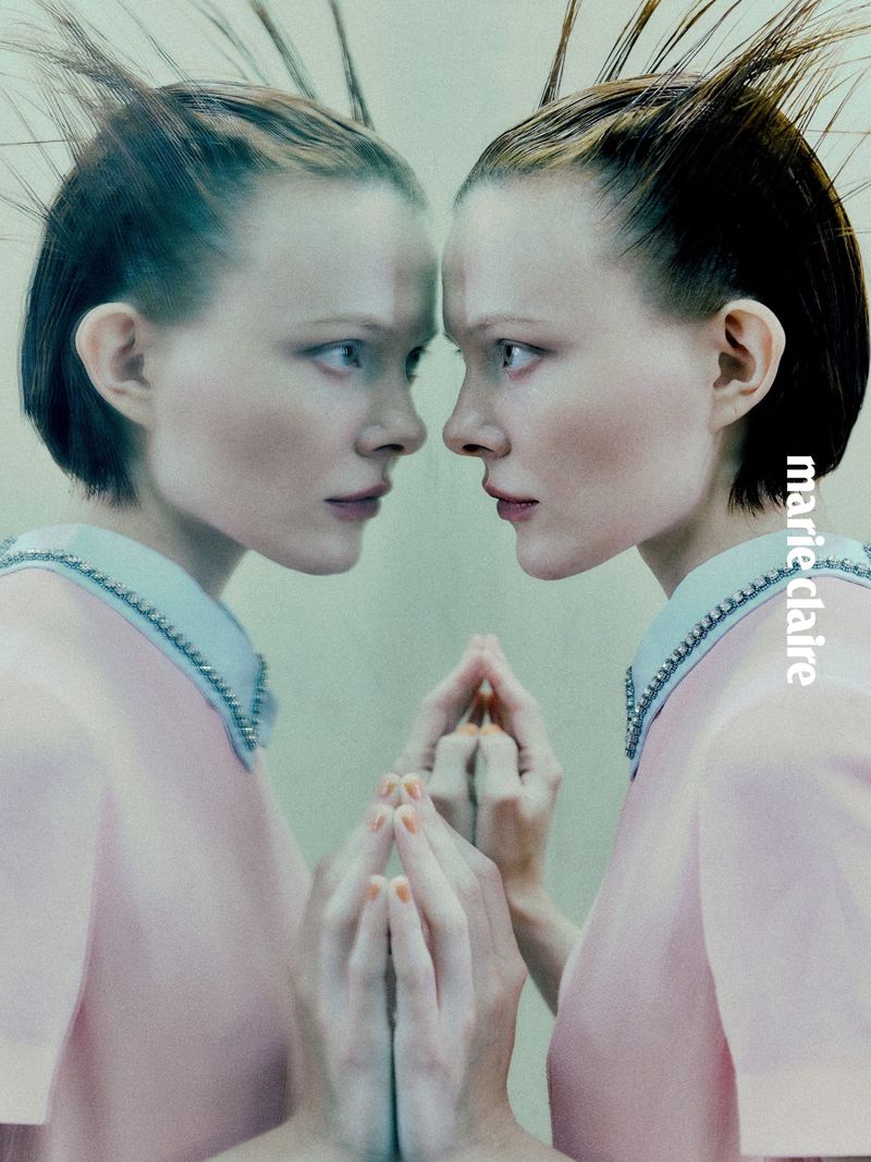 Fashionable woman in pink dress gazes into reflection, close-up studio shot, edgy hairstyle, pale skin, Marie Claire logo on the right.
