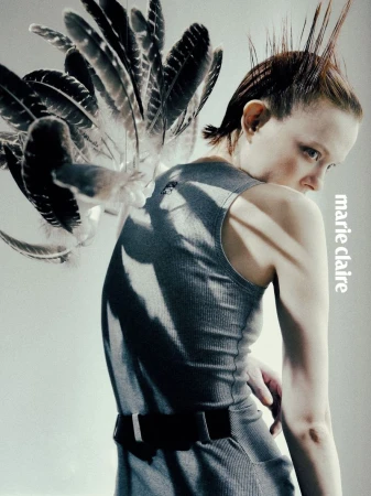 Fashion editorial shot of a woman in a grey dress and spiky hair, feathers accenting her shoulder, looking over her shoulder.