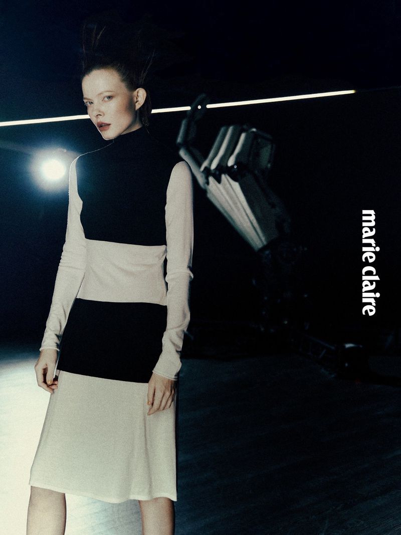 A fair-skinned woman with spiky hair poses in a color-blocked dress with a robot arm against a dark backdrop for Marie Claire.