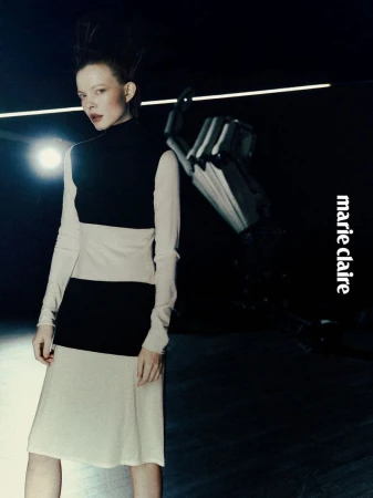 A fair-skinned woman with spiky hair poses in a color-blocked dress with a robot arm against a dark backdrop for Marie Claire.