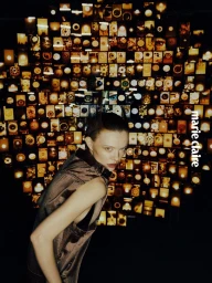 Model Sabi Khazgaleeva posing in a bronze metallic sleeveless top in front of an illuminated collage wall for Marie Claire Taiwan.