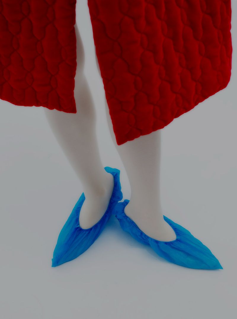 Close-up studio shot of an unrecognizable person wearing red culottes, white tights, and blue shoe covers on a light background.