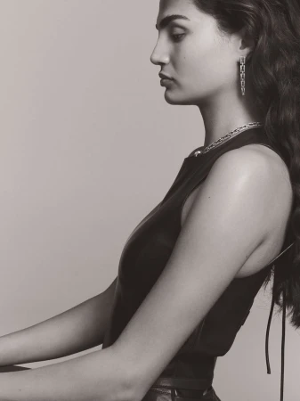 Profile portrait of a woman wearing fine jewellery including drop earrings and a necklace against a plain grey background