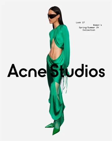 Fashion editorial shot of a woman in a green dress with a cutout, wearing black sunglasses, posing against a white backdrop.