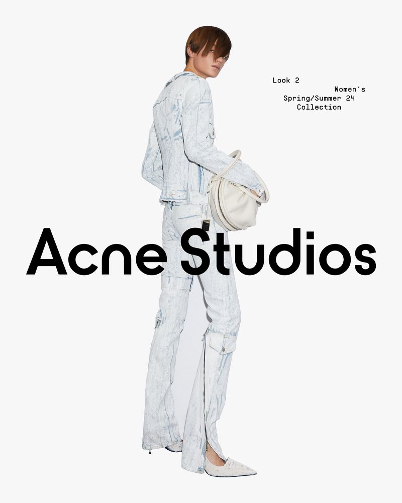 Fashion model in light blue denim jacket and trousers carries a white bag in a minimalist studio shot. 'Acne Studios' branding.