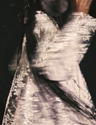 Model wearing an intricate floral patterned garment with dynamic motion blur against a dark black background.