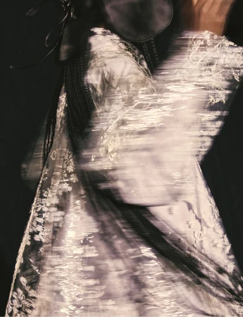 Abstract fashion image with a blurred woman in a floral dress and dark headpiece against a dark background, creating a dreamy effect.