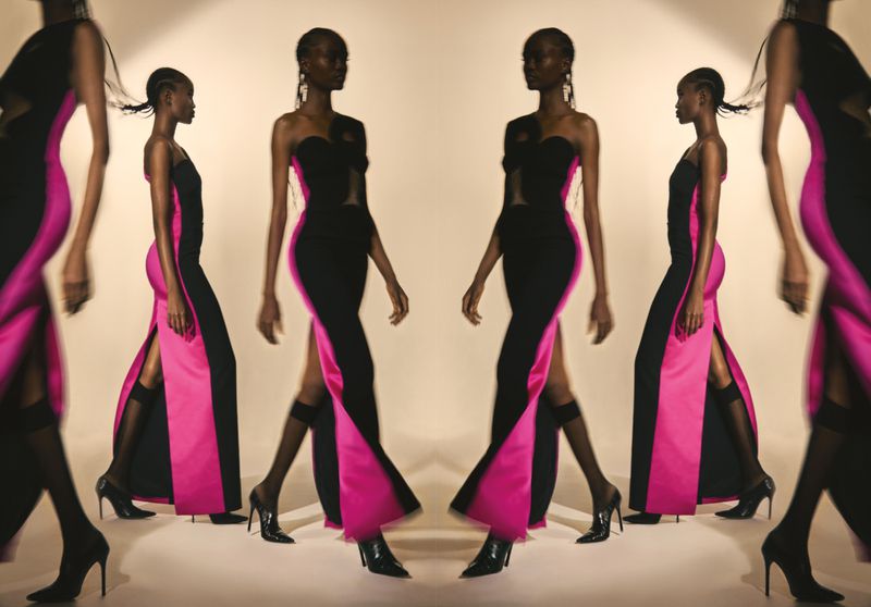 Elegant Black woman showcases a striking strapless black gown with a bold pink panel and thigh-high slit, complemented by sleek black heels.