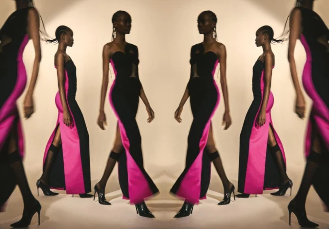 Elegant Black woman showcases a striking strapless black gown with a bold pink panel and thigh-high slit, complemented by sleek black heels.