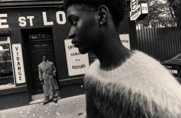 Monochrome portrait of two Black men in an urban setting, one wearing a coat, the other a sweater, with a vintage aesthetic.