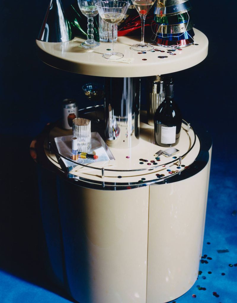 Celebratory drinks and party hats on a round bar cabinet with confetti on a blue floor in a brightly lit indoor setting.