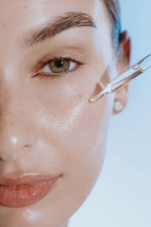Close-up of a woman's face as serum is applied to her cheek with a dropper, showcasing beauty, skincare, and cosmetic treatments.