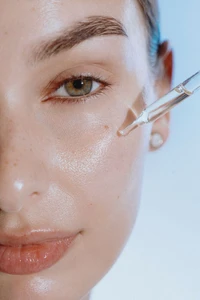 Close-up portrait of a woman's face receiving facial serum from a glass dropper during a skincare shoot.