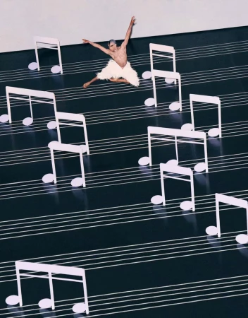 Male dancer in white costume leaps on a stage with music note props and black and white stripes mimicking sheet music.