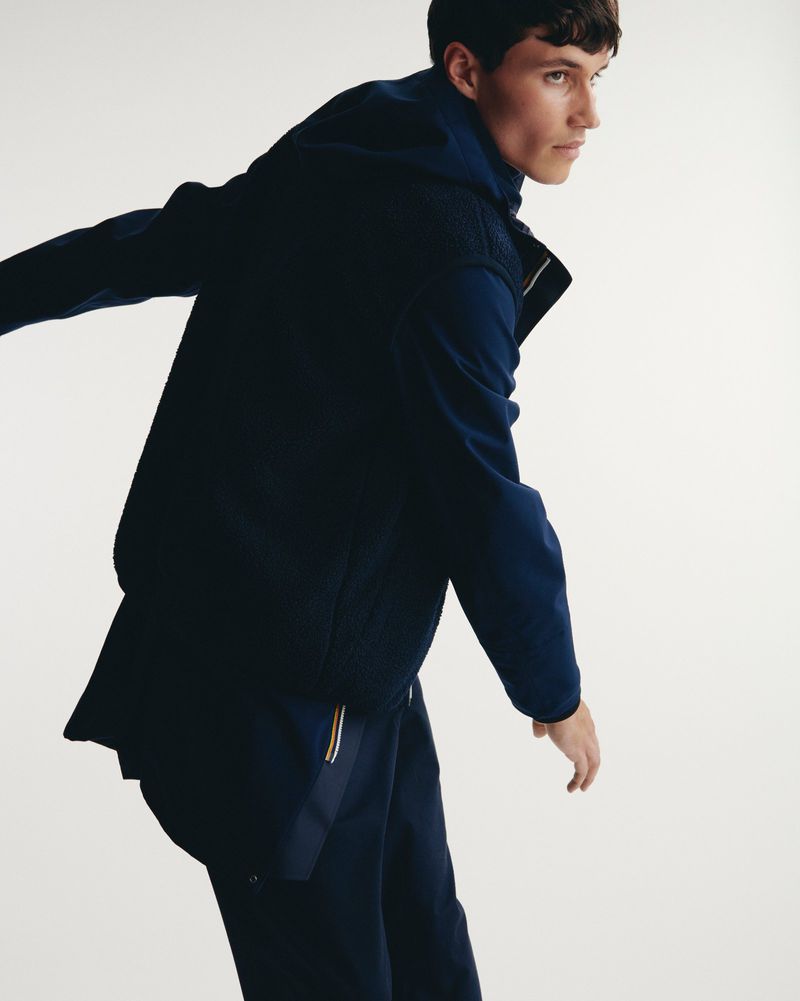 Man wearing a navy hooded jacket and matching pants against a plain white studio background