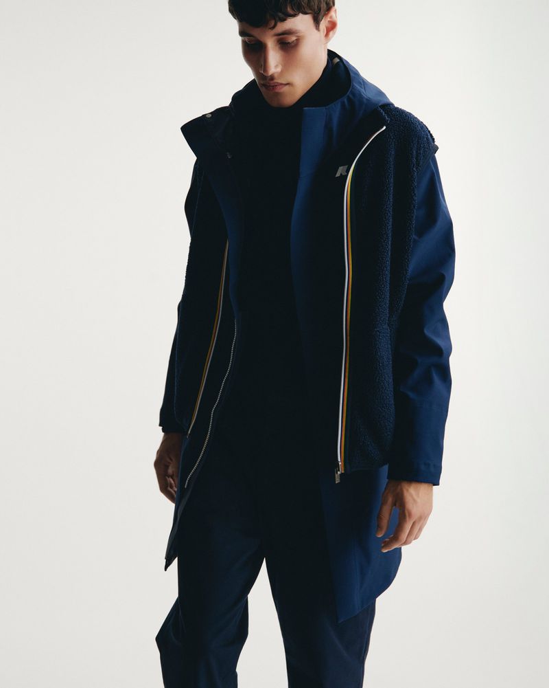 Man poses indoors wearing dark navy rain jacket with sherpa lining and matching pants in a studio setting, looking down.