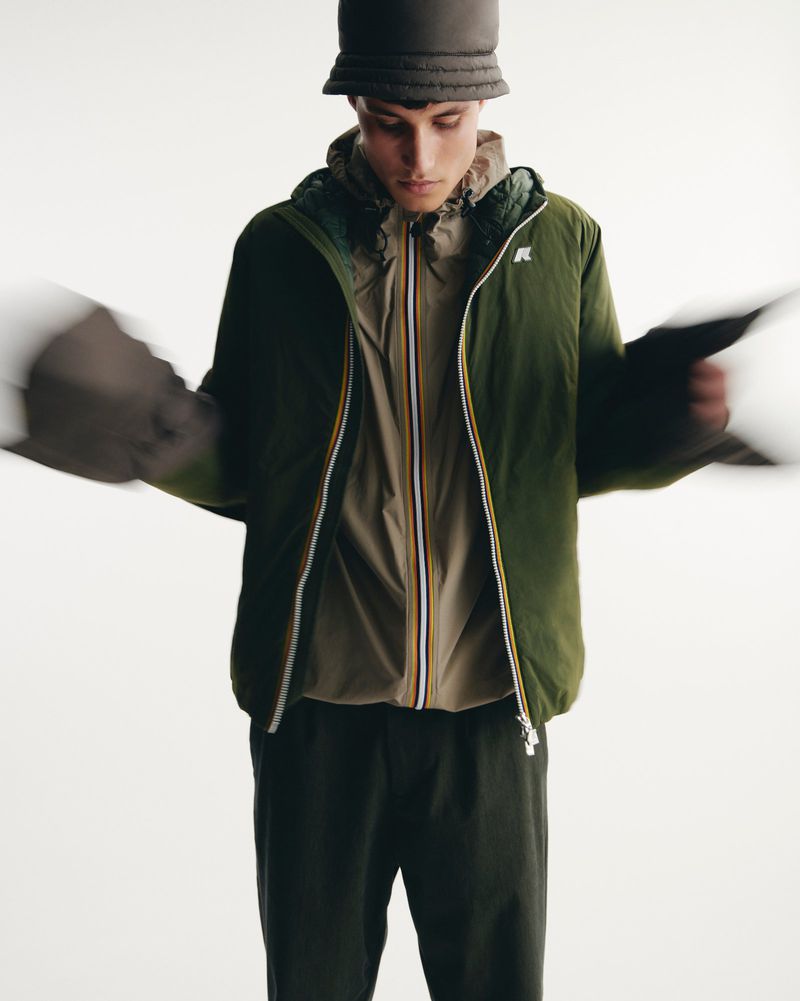 Male fashion model poses in a green jacket and bucket hat in a bright photo studio, showcasing neutral and earth-tone hues.