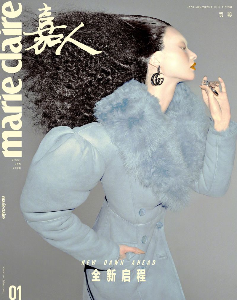 Magazine cover featuring a fashion model with dark, voluminous hair wearing a light blue coat and large earrings, set against a grey background.
