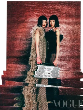 Two women in fashionable outfits pose indoors with a boombox, against a red textured backdrop in a Vogue fashion editorial.