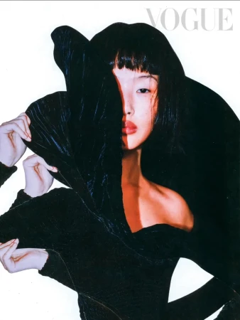 Asian woman with bold makeup partially obscured by black, draped, textured clothing against a stark white background for a magazine cover.