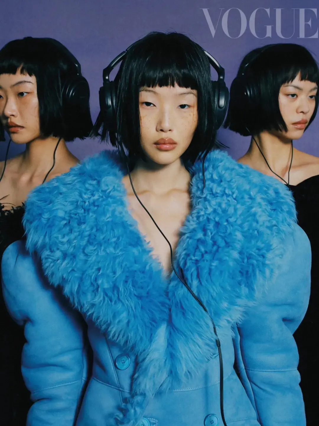 Fashion editorial featuring an Asian woman in a bright blue fur-collared coat and headphones, posing with two mirrored images of herself.