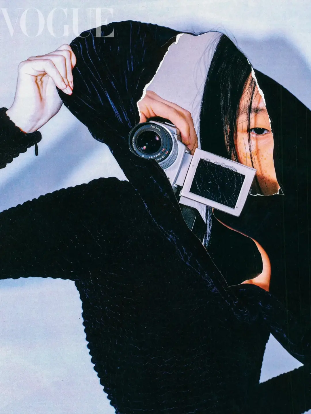 Fashion editorial featuring a woman with dark hair in a hooded outfit holding a camera in a collage-style Vogue magazine cover.