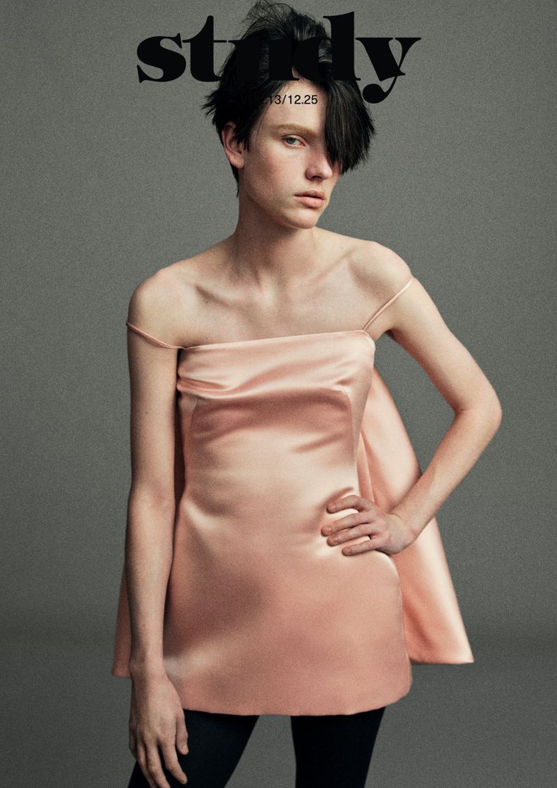 Fashion editorial portrait of a model wearing a pink dress with a modern hairstyle, set against a neutral grey background.