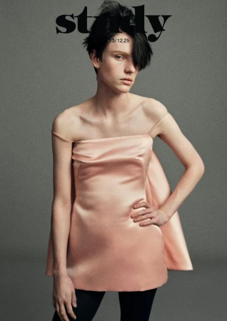 Fashion editorial portrait of a model wearing a pink dress with a modern hairstyle, set against a neutral grey background.