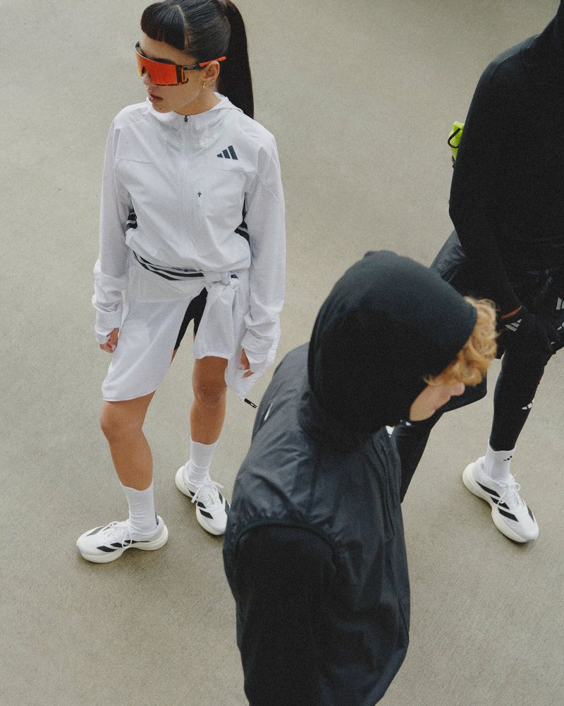 Three athletic models in white and black Adidas activewear, shot from above, showcase high-performance sportswear and sleek, modern designs.