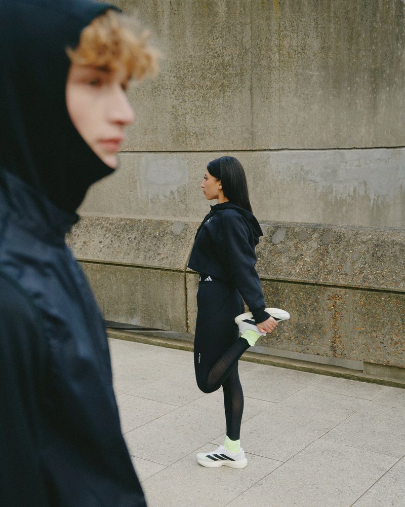 Two athletic adults in sportswear stretch outdoors against a textured concrete wall, embodying fitness and an active lifestyle.